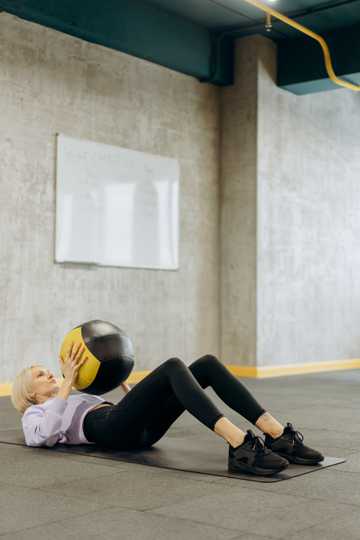 女人抱球躺在瑜伽垫上运动图片